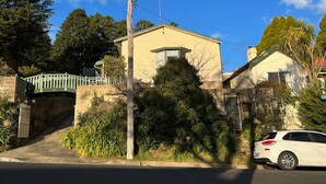 Une maison d’habitation avec un pont végétalisé, une voiture blanche garée devant, et un ciel bleu dégagé.