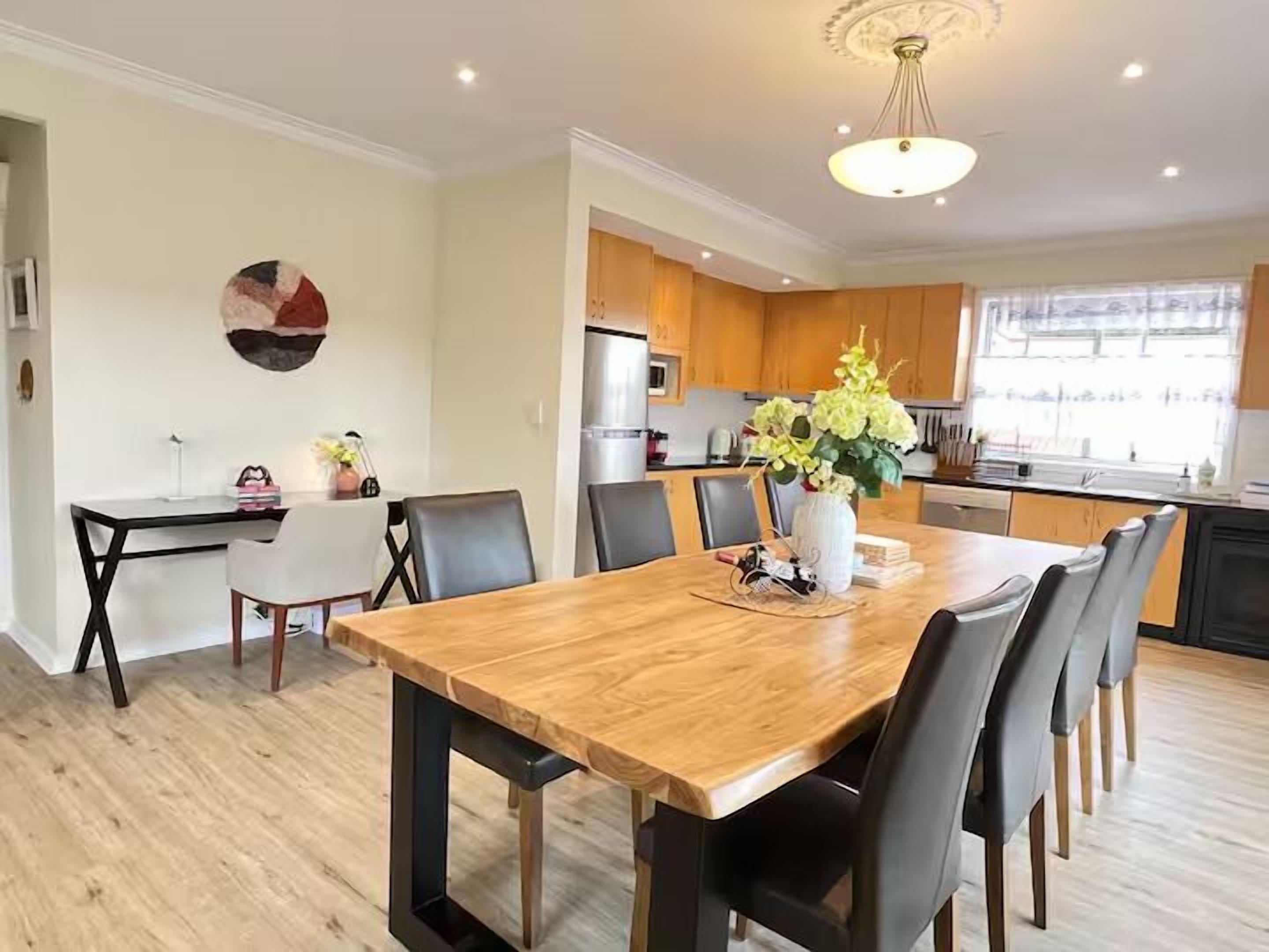A modern kitchen with wooden cabinets, a central island, and a dining area with a wooden table and chairs.