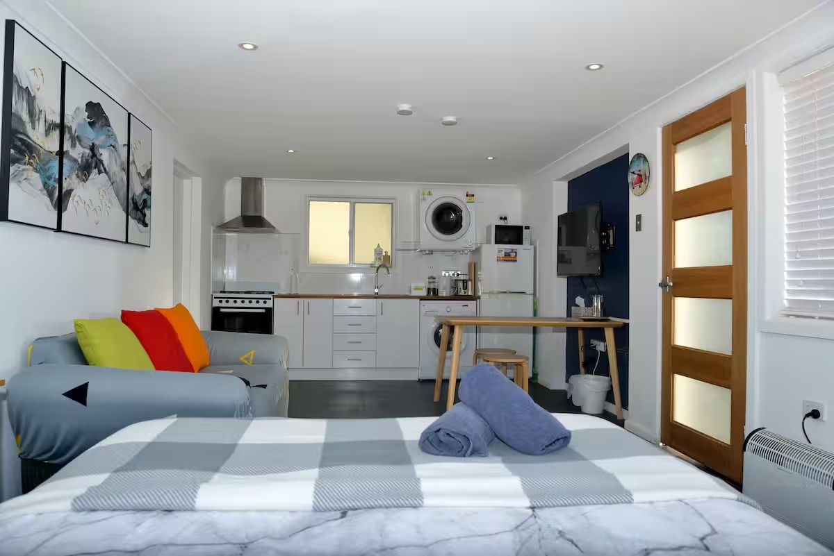 A compact hotel room with a bed, a kitchenette, a small dining table, and a bathroom.