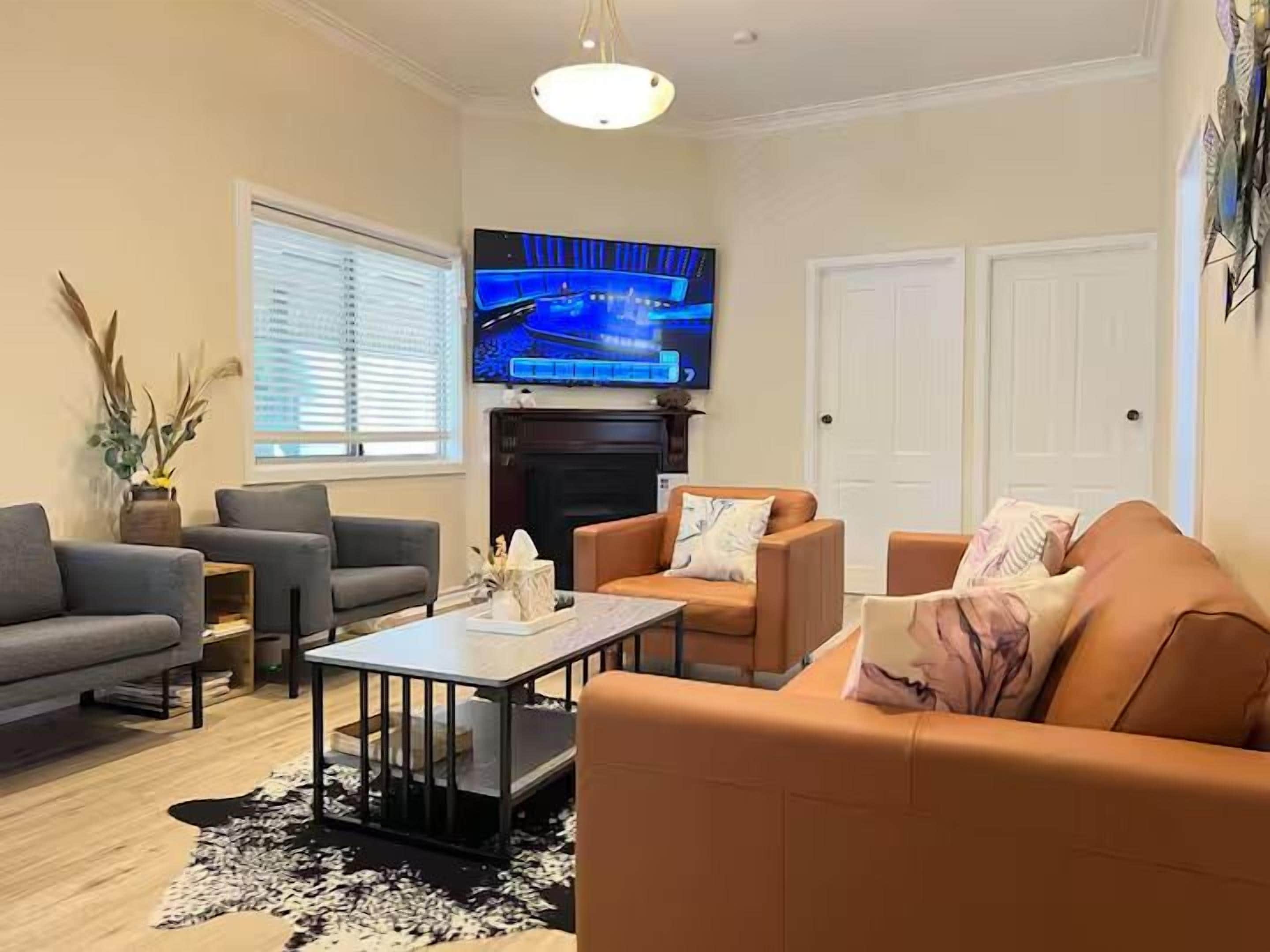 A living room with a sofa, armchairs, a coffee table, and a flat-screen TV mounted above a fireplace.