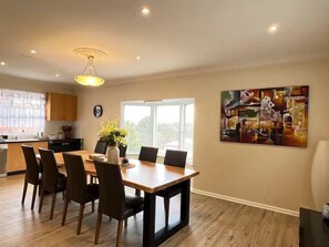 A modern dining area with a wooden table and chairs, a vase with flowers, and a large abstract painting on the wall. - Cozy Mountain Cottage (Katoomba)