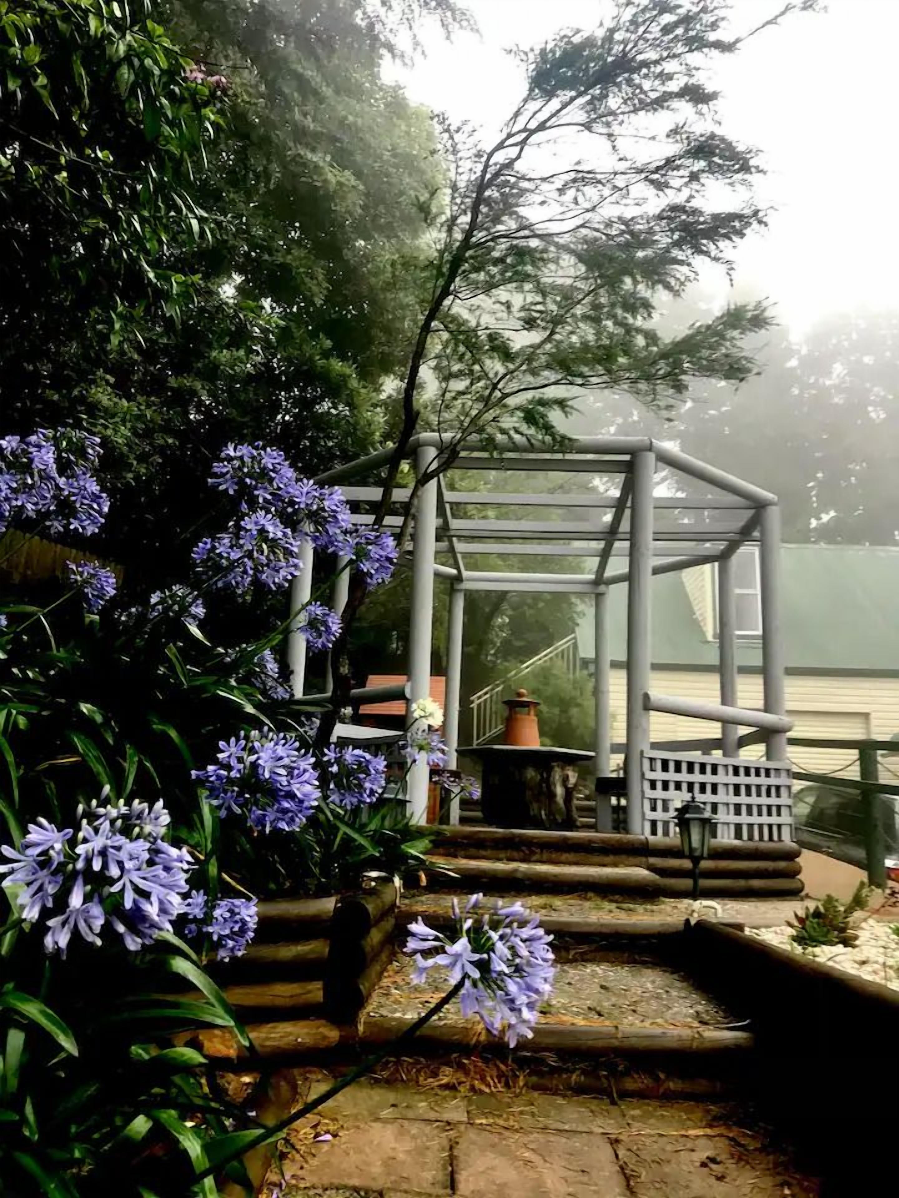 A garden with a gazebo, a small pond, and purple flowers.
