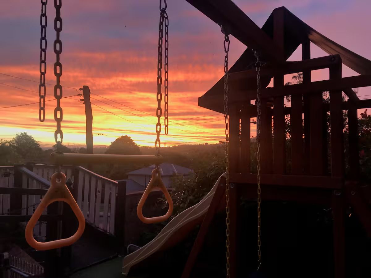 A playground with swings and a slide, set against a sunset sky.