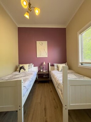 A room with two beds, a nightstand, a lamp, and a wall-mounted artwork. - Cozy Mountain Cottage (Katoomba)