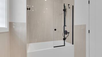 A modern bathroom with a glass-enclosed shower, a white bathtub, and a minimalist design.