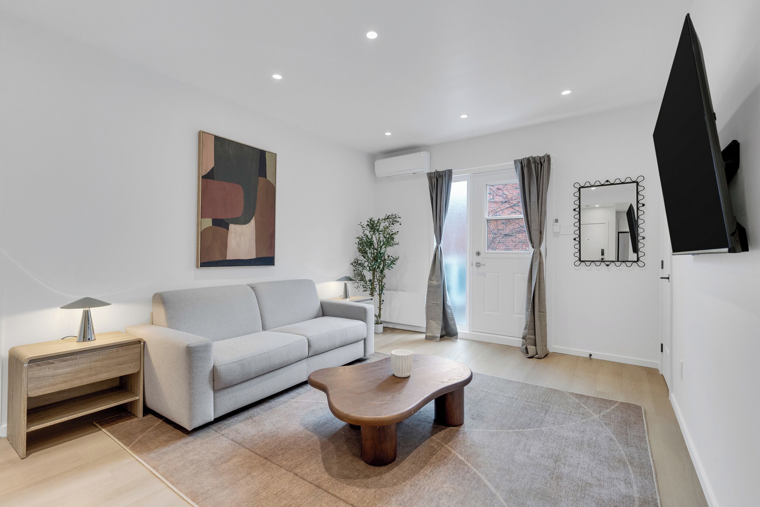 A modern living room with a grey sofa, wooden coffee table, and a painting on the wall.
