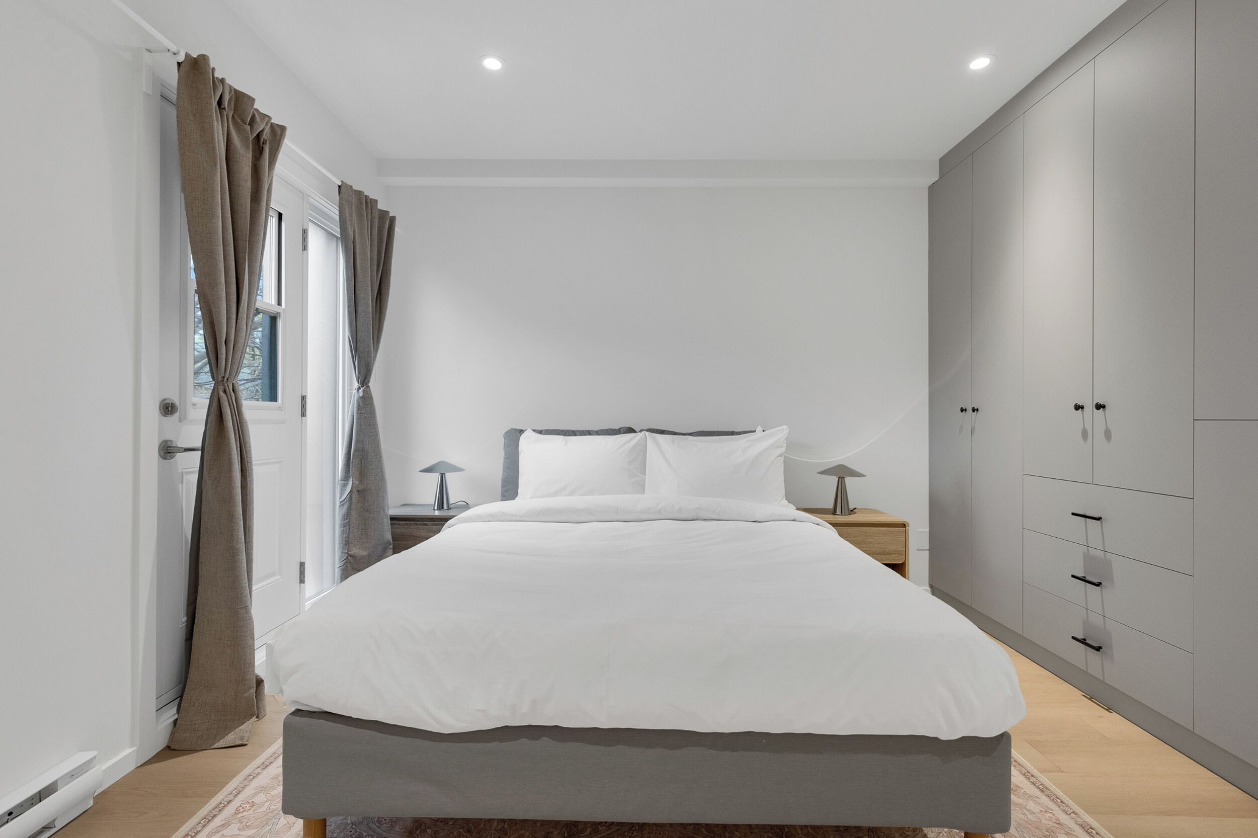 A modern bedroom with a large bed, a wardrobe, and a nightstand with a lamp.