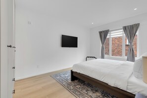 A bedroom with a bed, a TV mounted on the wall, and a window with curtains. - Le Victoria MidTown Montreal (Montréal)