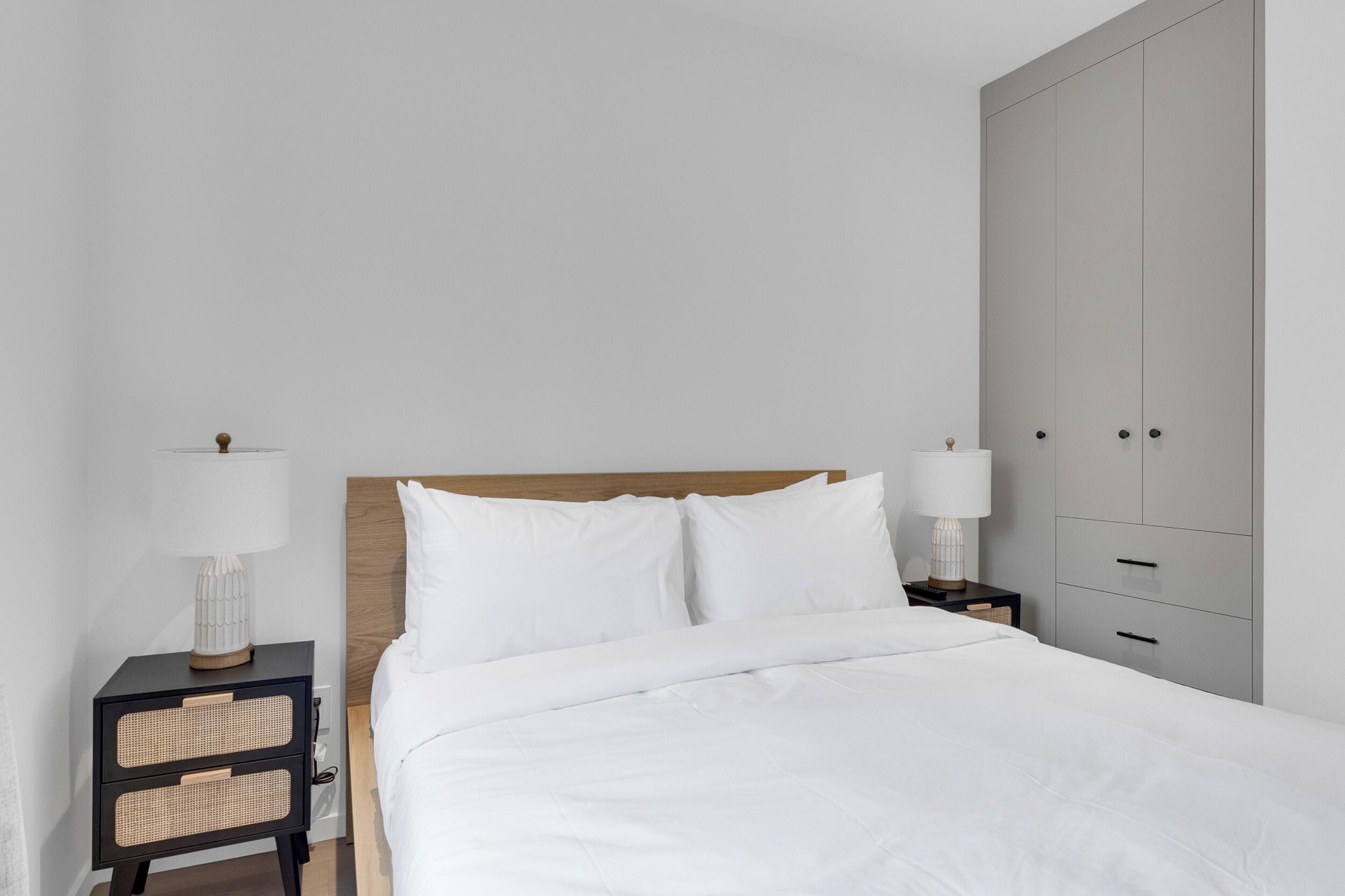 Une chambre à coucher au style minimaliste, comprenant un lit, deux tables de chevet avec des lampes, une armoire et une tête de lit en bois.