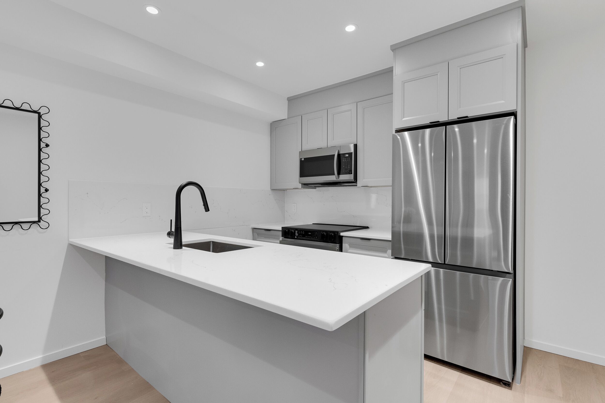 A modern kitchen with white cabinetry, a stainless steel refrigerator, a microwave, and a black faucet.