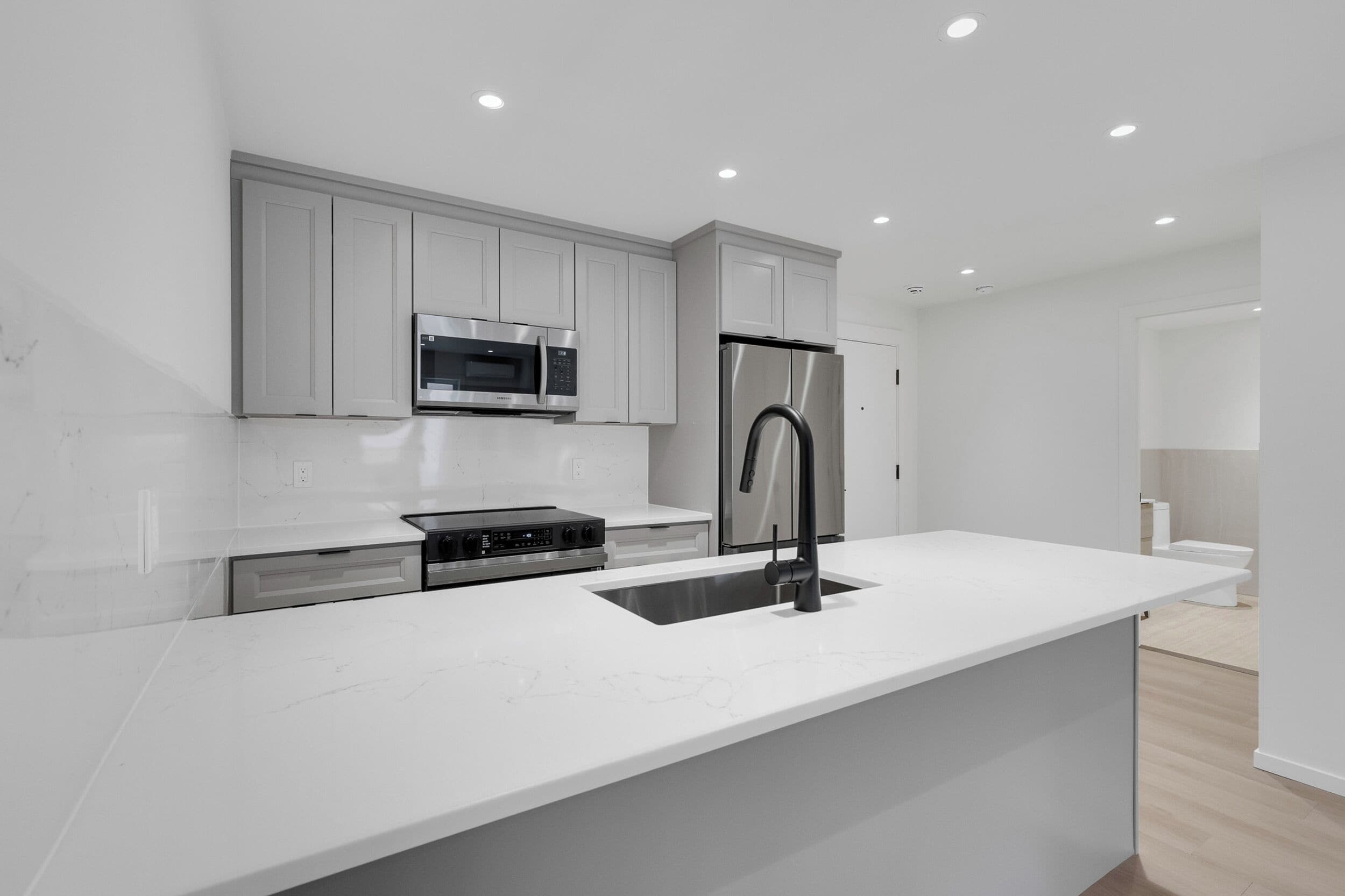 A modern kitchen with white cabinetry, stainless steel appliances, and a large island with a sink.