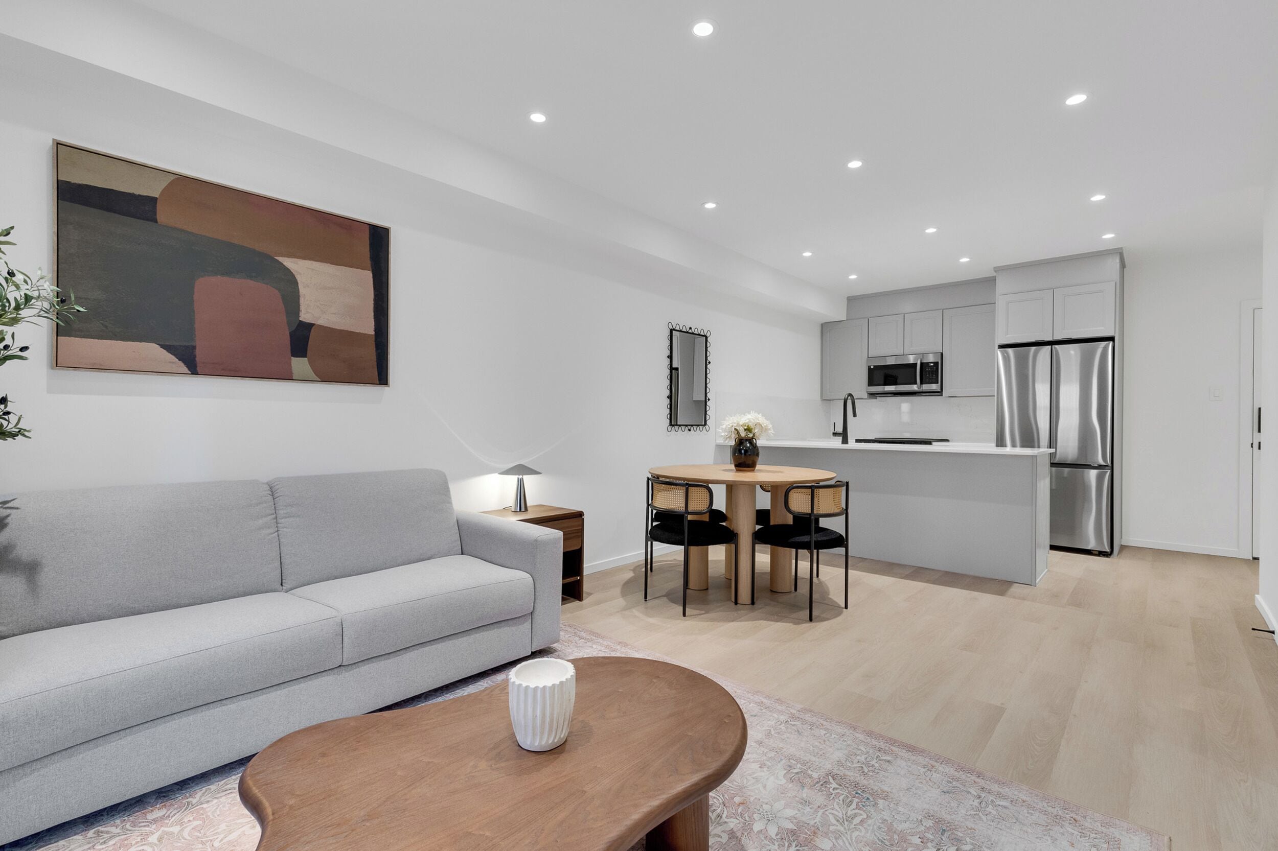 Ein modernes Wohnzimmer mit einem grauen Sofa, einem Holztisch und einem Bild an der Wand.