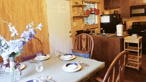 Un coin repas avec une table dressée pour deux personnes, des meubles en bois, un réfrigérateur et une fenêtre avec des rideaux.