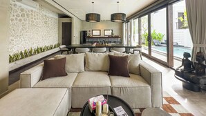 A modern living room with a sofa, coffee table, and a dining area with a TV. - Iri Villas Ubud  (Kemenuh)