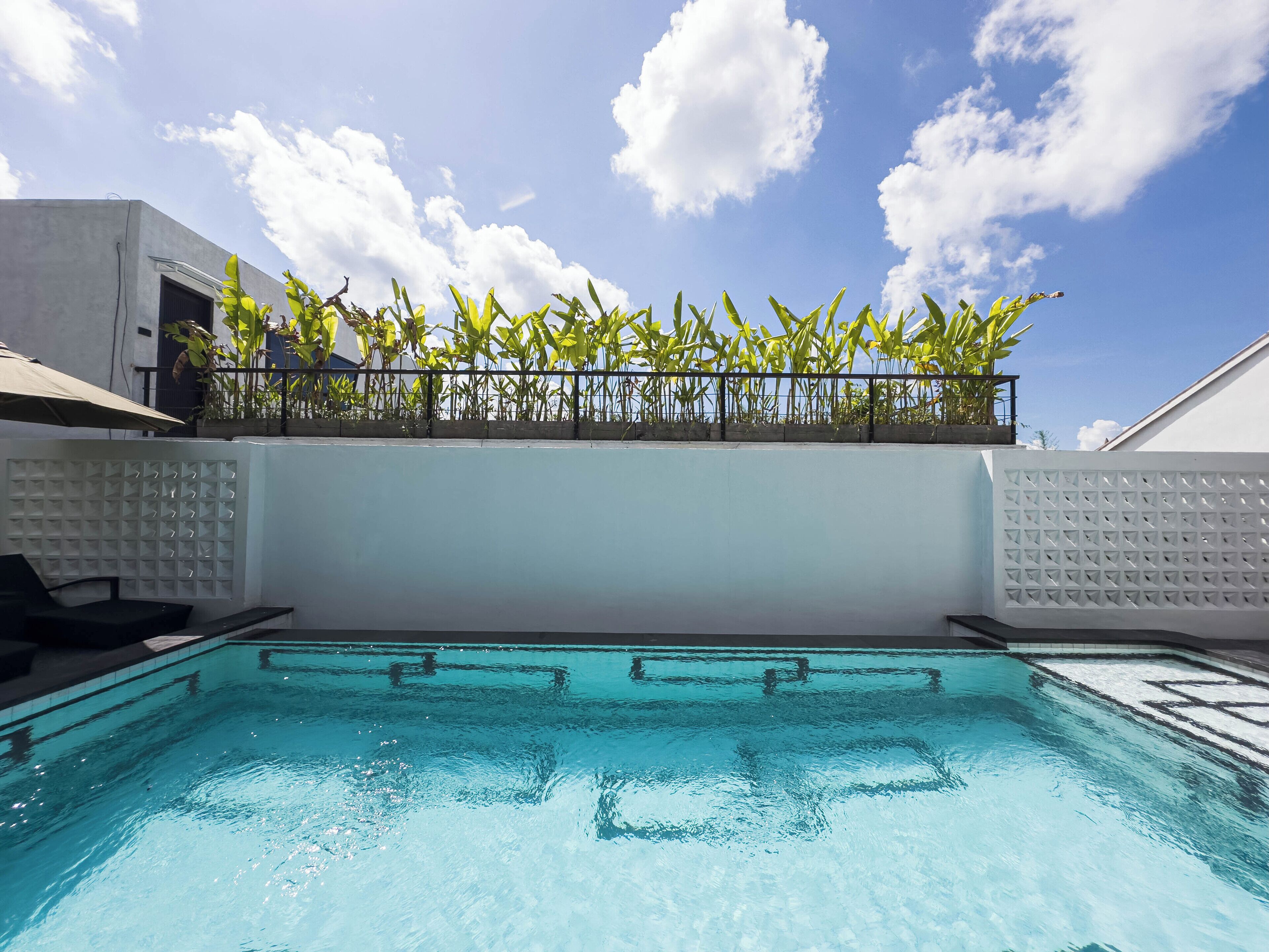 A swimming pool with a clear blue water surface, surrounded by a white wall and a metal railing.