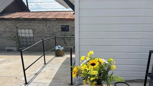 Een ronde tafel met een mand vol gele bloemen, op een betonnen terras, met een metalen hek op de achtergrond.