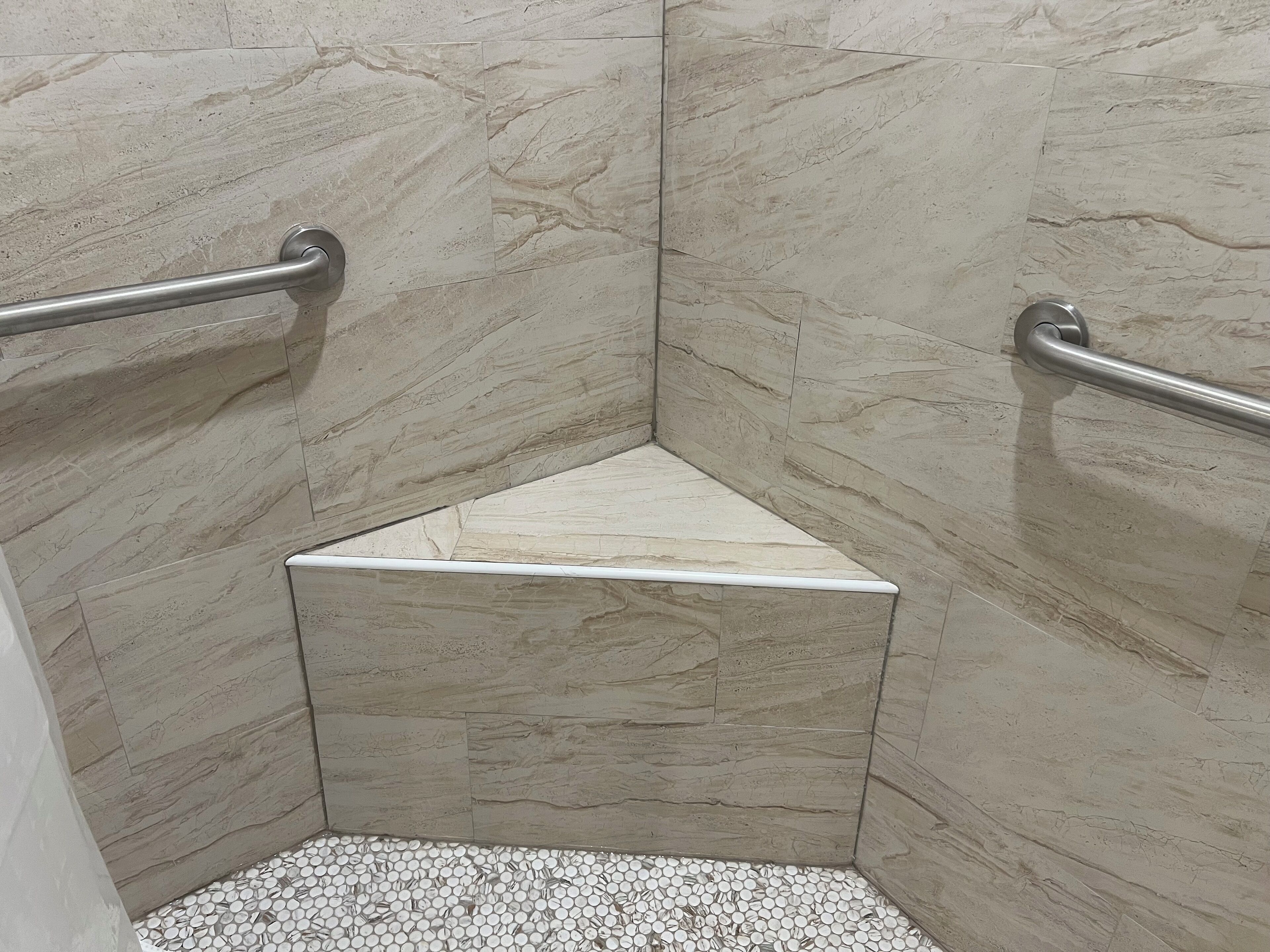 A corner shower with marble walls and a white tiled floor.