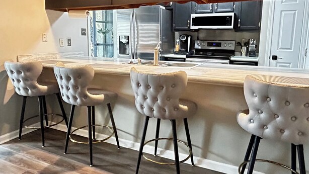 Cozinha moderna com área de bar, apresentando eletrodomésticos de aço inoxidável, armários escuros e banquetas estofadas.