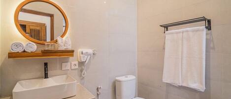 Un baño moderno con un espejo ovalado grande, un lavabo blanco, un inodoro y un perchero para toallas.