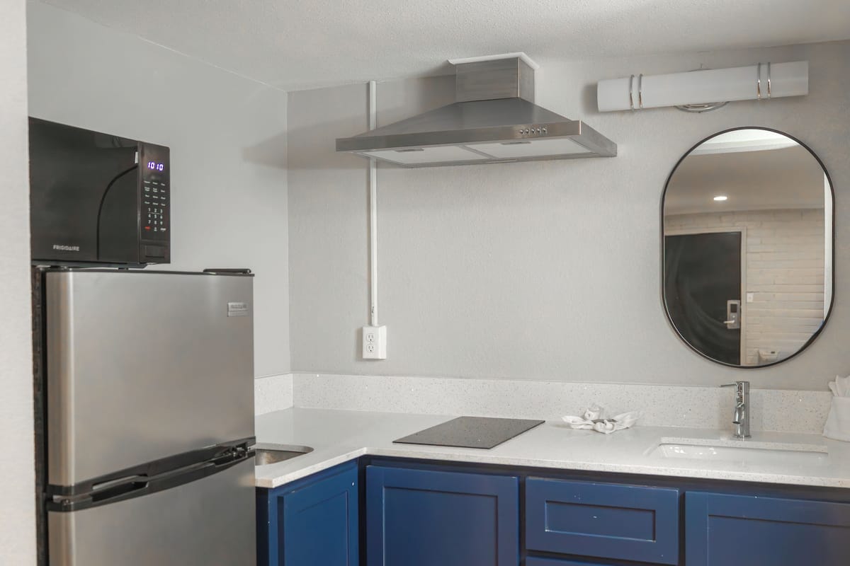 Una cocina con refrigerador de acero inoxidable, microondas, campana extractora a gas, pileta y grifería, y alacenas azules.