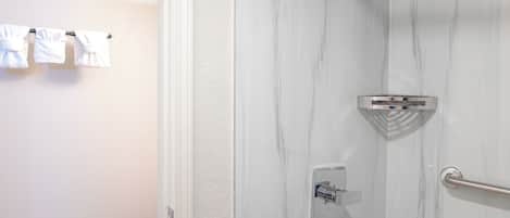 A bathroom with a shower, a towel rack with towels, and a wooden floor.