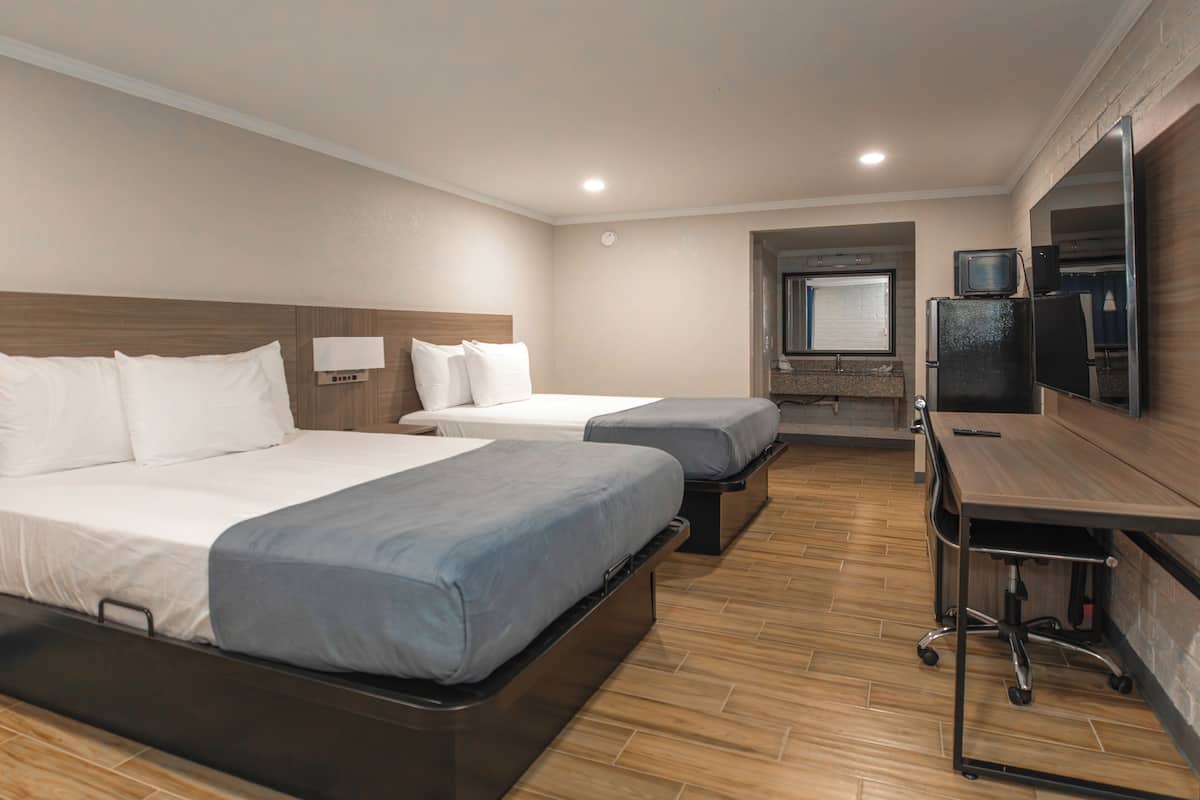 Habitación de hotel con dos camas, un escritorio, un televisor y una ventana pequeña.