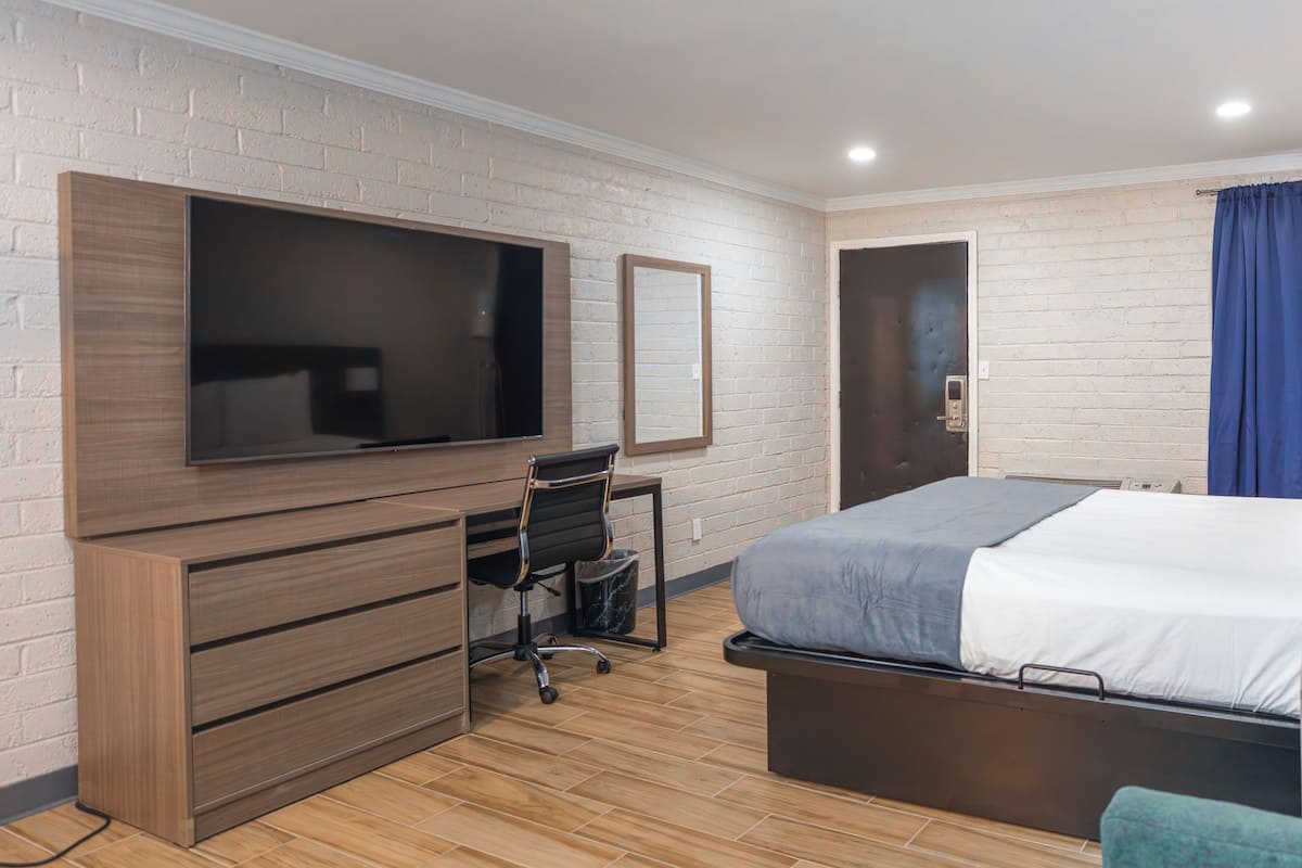 Una habitación de hotel con cama, escritorio con silla, televisor montado en la pared y una puerta.