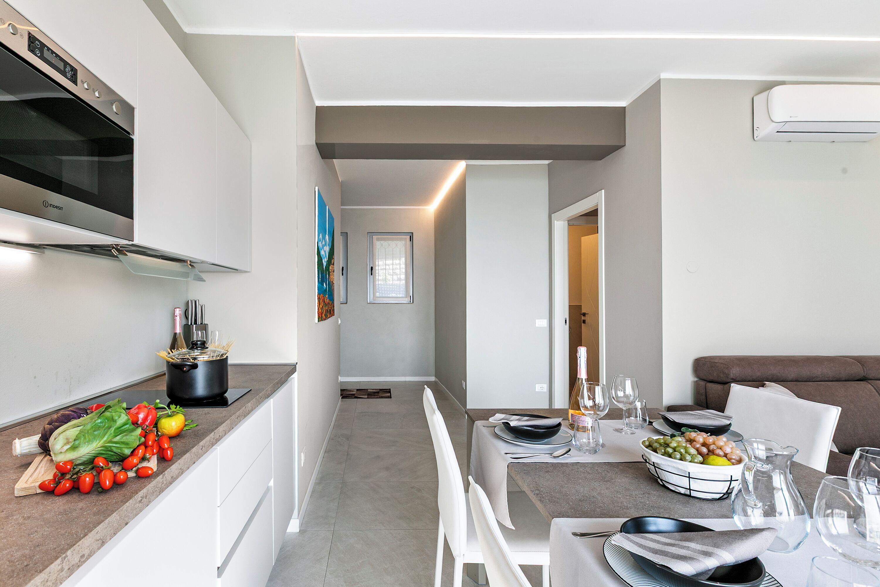 A modern kitchen with a built-in oven, a dining area with a table set for two, and a living area with a sofa.