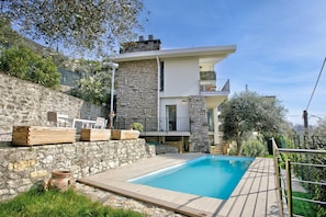 A modern house with a stone facade, a swimming pool, and outdoor furniture.