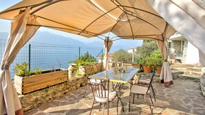 Un patio al aire libre con una mesa y sillas, un paraguas grande y vistas al mar y a las montañas.