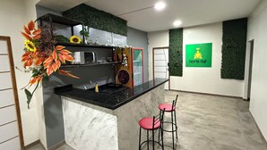 A modern kitchen with a marble countertop, a built-in microwave, and a sink. There are two red bar stools and a decorative plant with orange leaves. A green sign with the text "Norte Hub" is on the wall. - Casa Paraense  (Manaus)