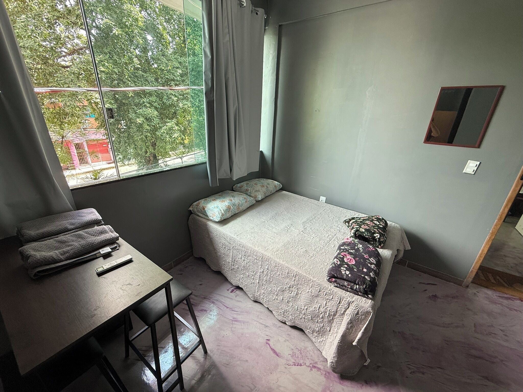 Una habitación pequeña con cama individual, ventana, escritorio y espejo.