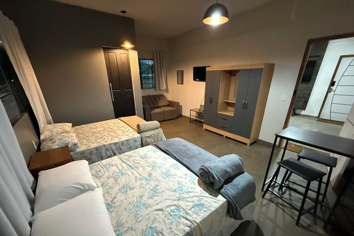Una habitación de hotel moderna con dos camas individuales, un sofá, una mesita pequeña y un armario.