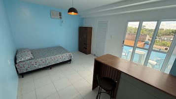 Una habitación con cama, escritorio, silla, armario y ventana con vista a edificios.