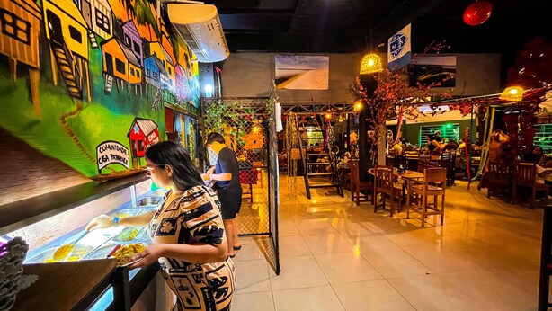 A restaurant with a colorful mural, a buffet counter, and a seating area with tables and chairs. - Casa Paraense  (Manaus)