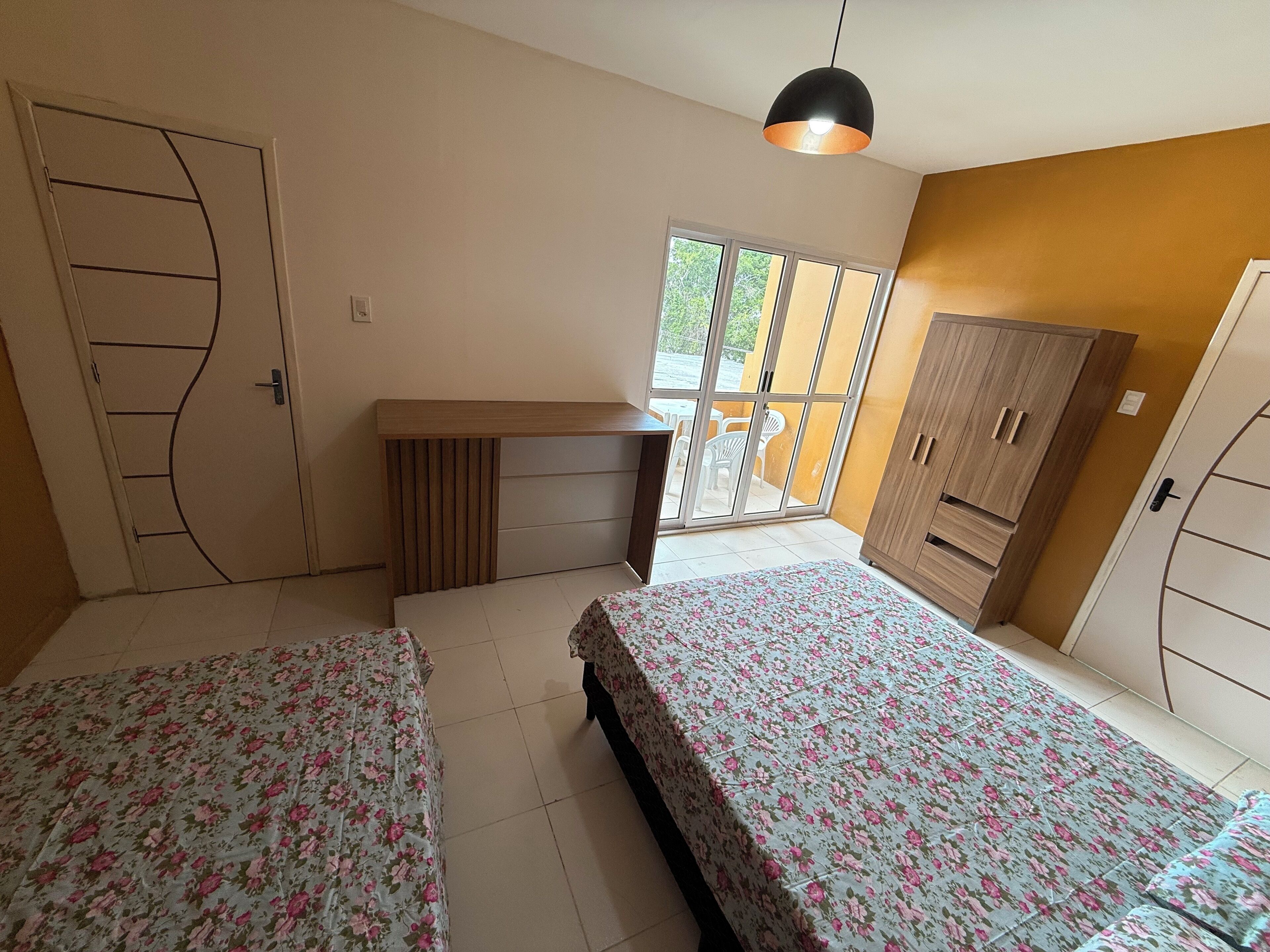 Un dormitorio con dos camas, un escritorio de madera, un armario y un ventanal corredero que da a un espacio exterior.