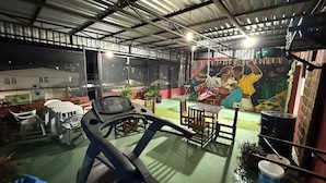 A covered outdoor area with a treadmill, a table with chairs, and a mural on the wall. - Casa Paraense  (Manaus)