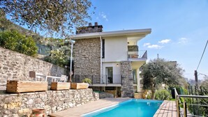 Una casa moderna de dos pisos con fachada de piedra, piscina y mobiliario exterior.