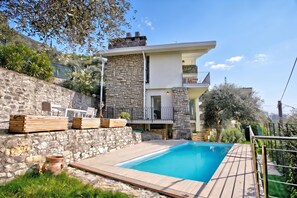 A modern two-story house with a stone facade, a swimming pool, and outdoor seating.