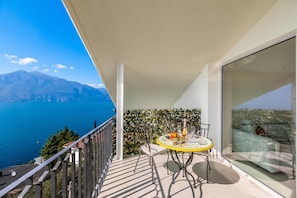 Un balcón con una mesa lista para comer, con vistas a un cuerpo de agua y montañas.