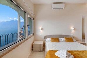 A hotel room with a bed, a nightstand, a window with a view of mountains, and an air conditioning unit.