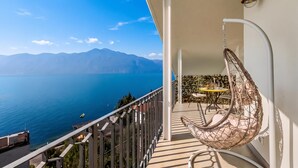 Un balcón con vistas al mar y a las montañas, una silla colgante y una pequeña mesa con una silla.