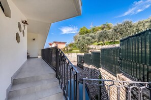 Propiedad residencial con balcón, pared de piedra y vistas a olivos y un edificio lejano.
