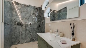 Un baño moderno con cabina de ducha de mármol, un lavamanos espacioso y un espejo sobre el lavamanos.
