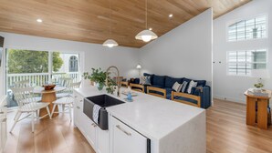 A modern kitchen with a central island, wooden ceiling, and large windows.