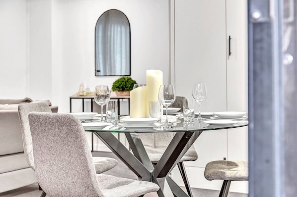 A modern dining area with a glass table set for four, surrounded by grey upholstered chairs. - Stellar Apartments 3 bedroom apartment with rooftopviews overlooking the city (Kent Town)