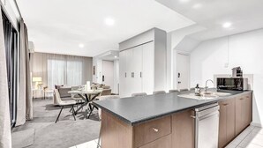 A modern kitchen with a central island, built-in cabinets, and a dining area with a table and chairs. - Stellar Apartments 3 bedroom apartment with rooftopviews overlooking the city (Kent Town)
