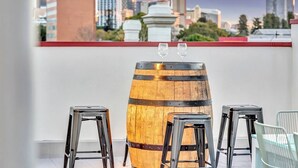 A rooftop terrace with a wooden barrel centerpiece, two stools, and a glass table. - Stellar Apartments 3 bedroom apartment with rooftopviews overlooking the city (Kent Town)