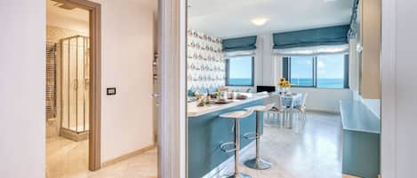 A modern kitchen with a bar area, a dining space, and a view of the sea.