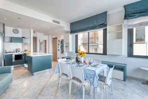 A modern kitchen with a central island, dining area with a table set for four, and a view of the balcony.